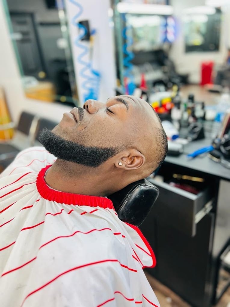 Man with dark beard tilting head back in a barbershop setting with equipment visible in background
