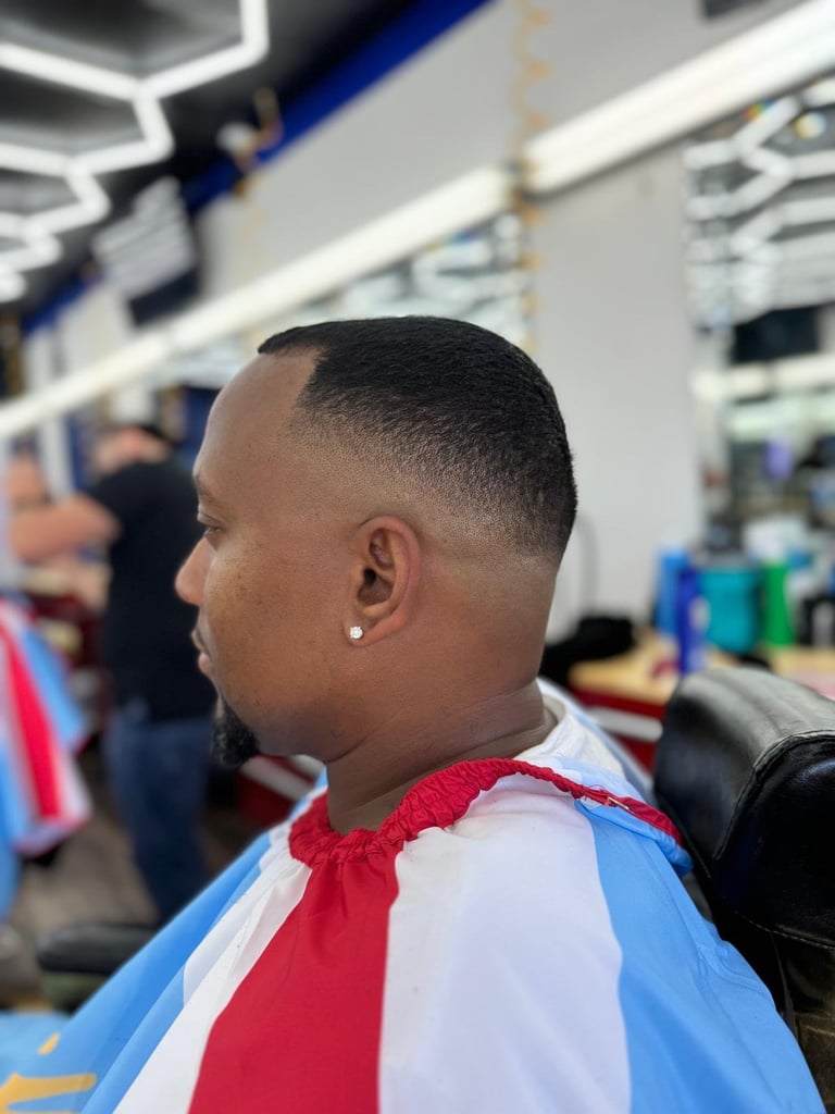 Man with short hair wearing red, white, and blue striped cape in barbershop setting